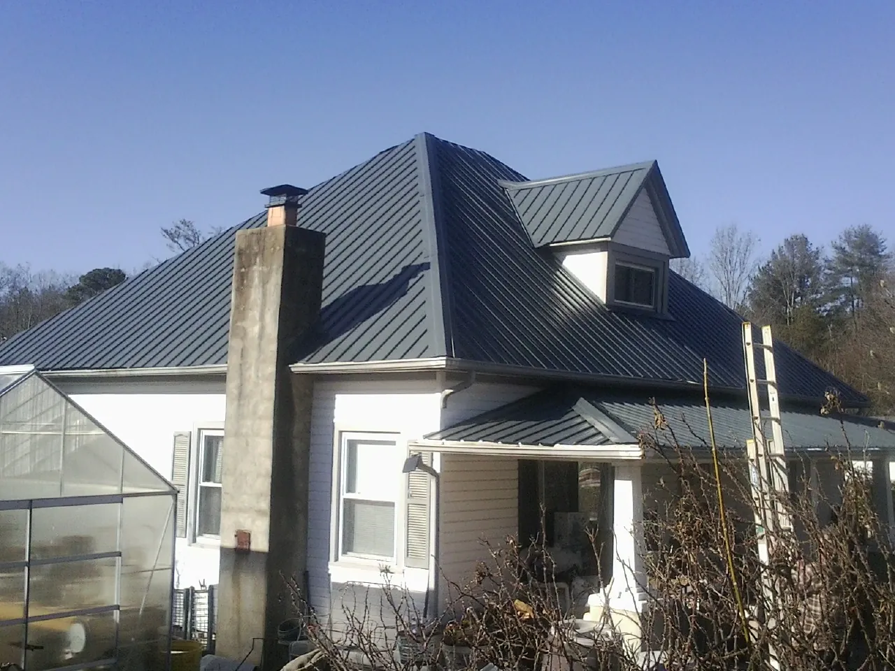 Dark blue standing seam metal roof on a white farmhouse with dormer — Slate & Tile Roof Repair by Roofing Brothers in Maple Valley