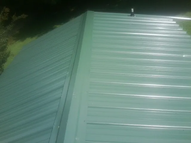 New green metal panels meeting at the ridge of a roof — Flat Roof Repair work by our crew in Maple Valley