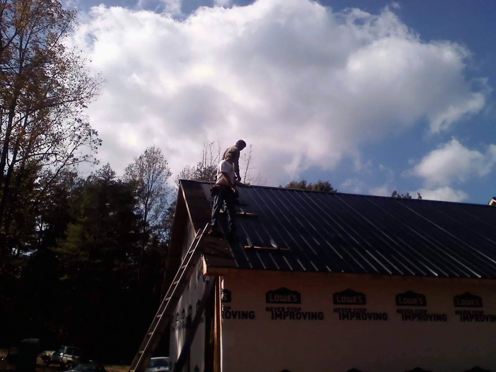 Roofer fastening dark metal panels high against a cloudy sky, from a Roof Inspection job in Maple Valley